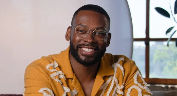 Smiling man with glasses and beard wearing a mustard yellow shirt with white patterns.